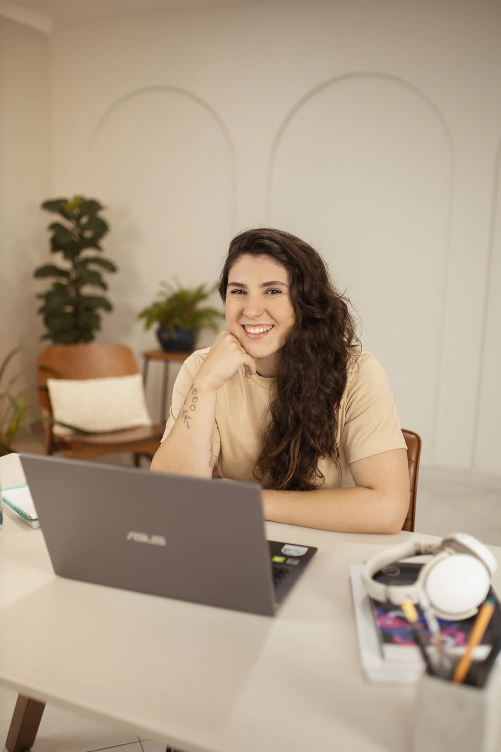 Ana Marques sorrindo à mesa de trabalho, com notebook e fone de ouvido, durante atendimento online